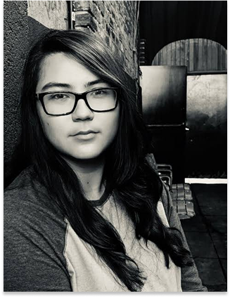 Black and white photo: long hair, thick rim sunglasses, an almost smile